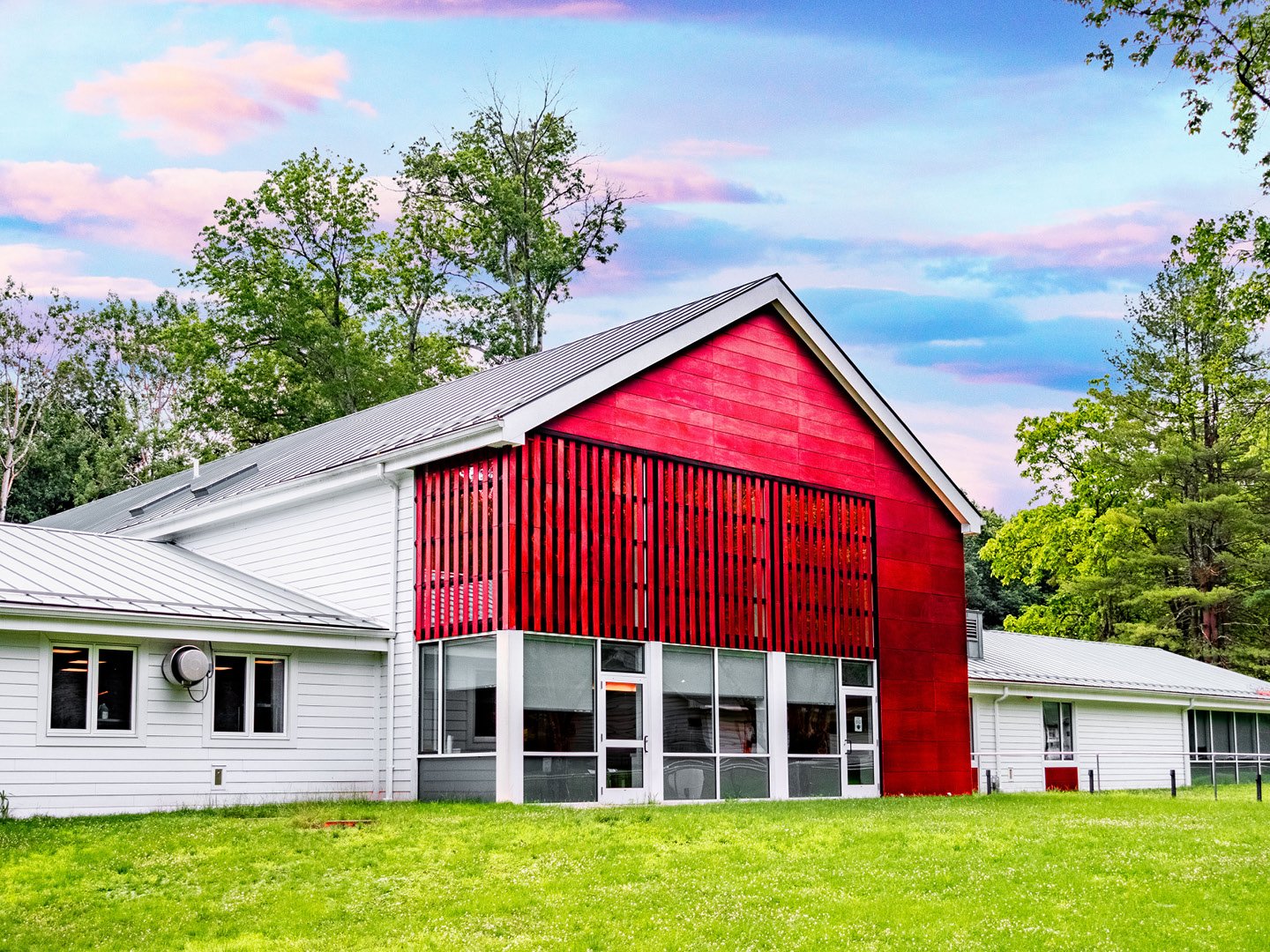 Photo of a large, red, barn-shaped building with a light gray roof, sitting on a green lawn.